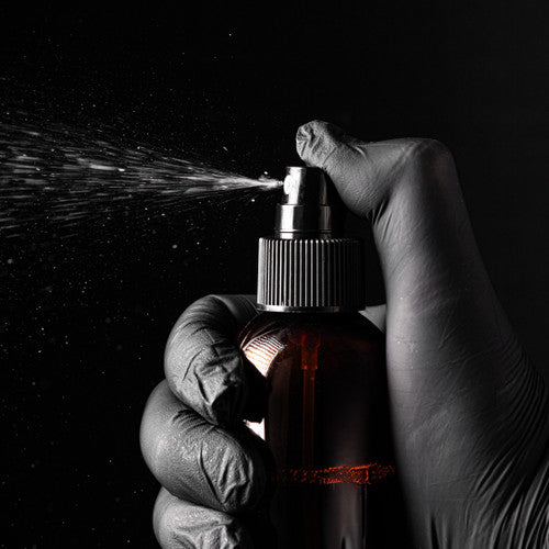 Hand wearing a glove holding a spray bottle with a dark background - Zoom Media 1