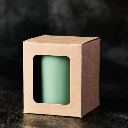 Green candle in a brown cardboard box with a window on a dark background - Zoom Media 1