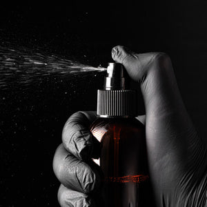 Hand wearing a glove holding a spray bottle with a dark background - Featured Image