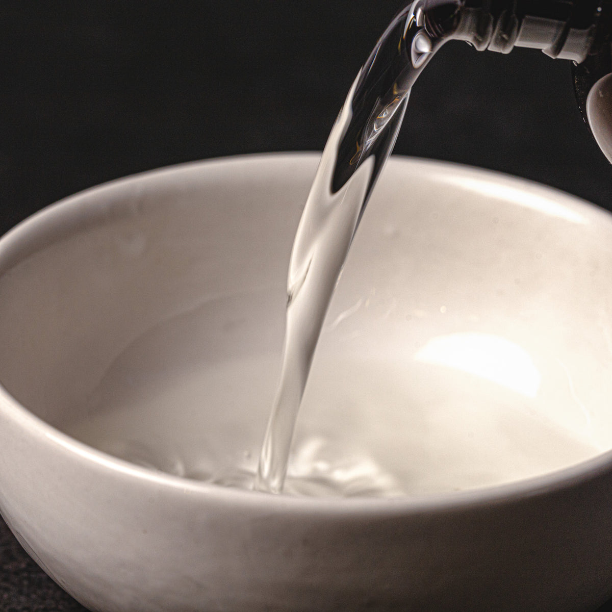Water being poured from a faucet into a white bowl on a black background