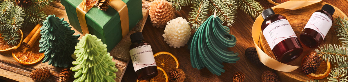 Christmas display with green tree-shaped candles, fragrance oil bottles, a wrapped green gift, evergreen branches, pinecones, cinnamon sticks, and dried orange slices on a rustic wooden surface.