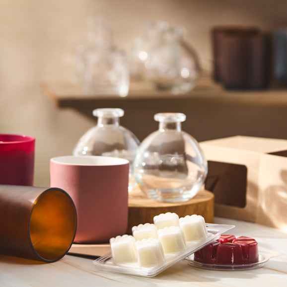 A collection of candle-making supplies including glass jars, colorful vessels, and wax melts displayed on a wooden surface, showcasing materials ready for crafting and packaging.
